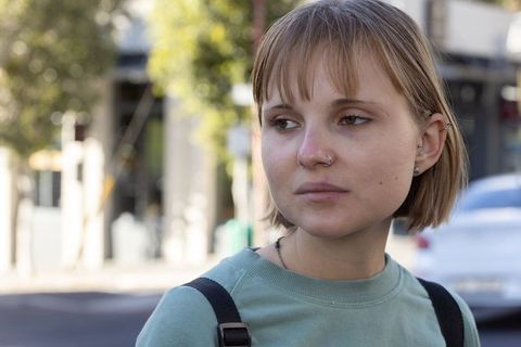 Pensive young woman with nose ring and backpack on urban sidewalk in daylight