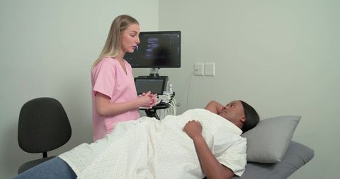 Sonographer consulting with african american patient during ultrasound exam in clinic room