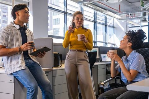 Coworkers chatting over coffee in modern open-plan office with city view building teamwork