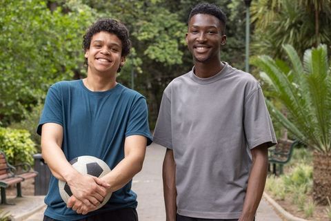 Two friends holding soccer ball smiling on park walkway casual athletic outdoor portrait