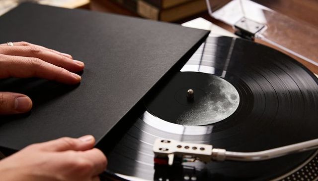 Sliding vinyl sleeve revealing moon label on vintage turntable with tonearm and hands