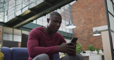 African American Man Engaging with Smartphone in Stylistic Office Lounge