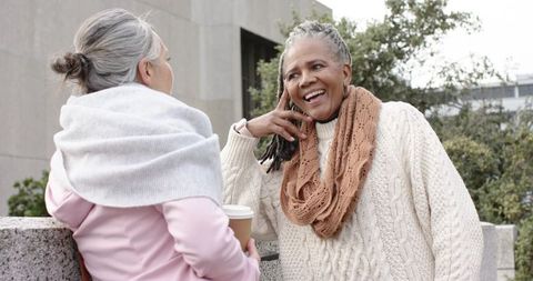 African american senior woman and friend chatting over coffee in urban courtyard