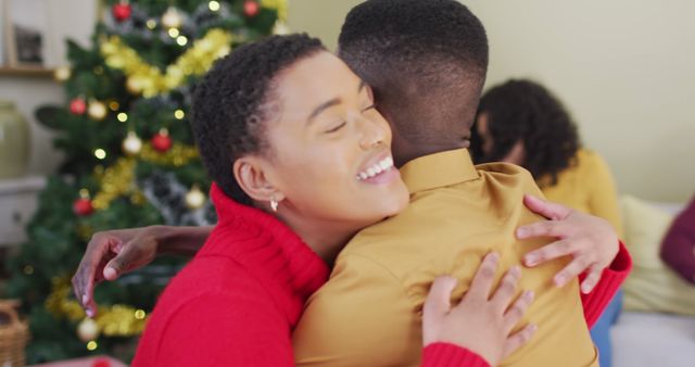 Happy diverse male and female friend hugging in front of christmas tree at home. christmas festivities, celebrating at home with family and friends.