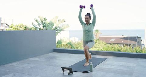 Woman exercising with dumbbells on rooftop terrace following online workout