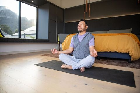 Asian mature man meditating in minimalist bedroom with mountain view and mustard duvet