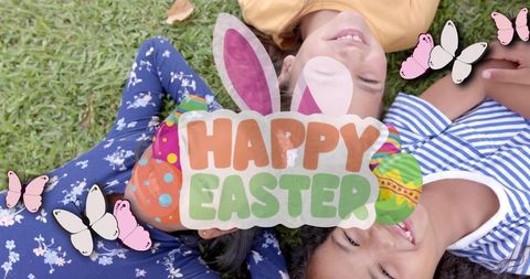 Three children lying on grass smiling with happy easter graphic, bunny ears, colorful eggs