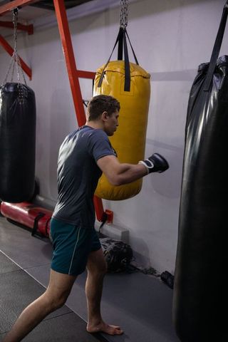 Mid-30s man training on suspended yellow heavy bag in boxing gym punching workout