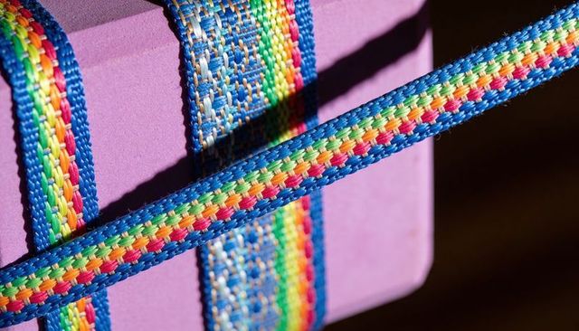 Bright rainbow braided nylon strap wrapping purple foam block with strong diagonal shadows