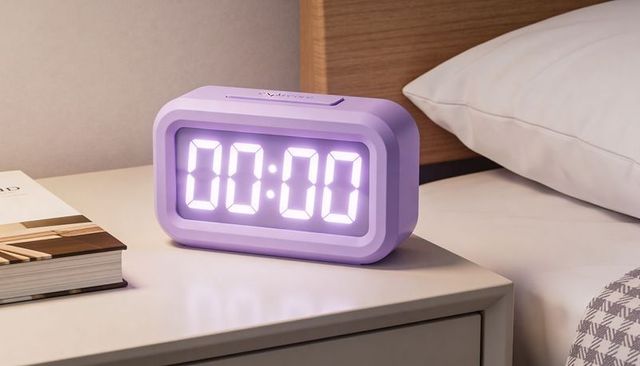Lavender digital alarm clock glowing 00:00 on bedside nightstand with cozy bedroom styling