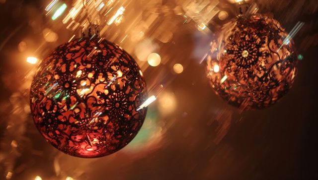 Glowing ornate filigree Christmas bauble casting warm bokeh light and metallic sparkle