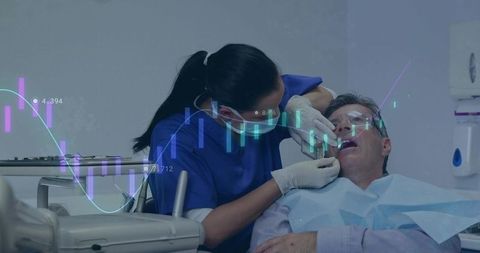 Dentist examining middle-aged male patient in dental chair with digital data overlay