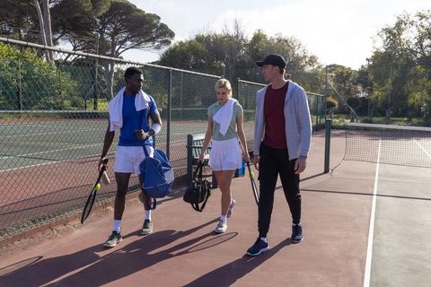 Walking off tennis court after match carrying rackets, bags and towels, enjoying camaraderie