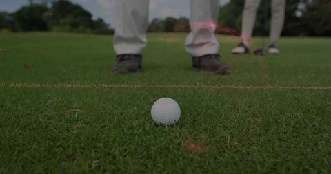 Close-up low-angle golf ball resting on tee with golfers' shoes and trousers on fairway