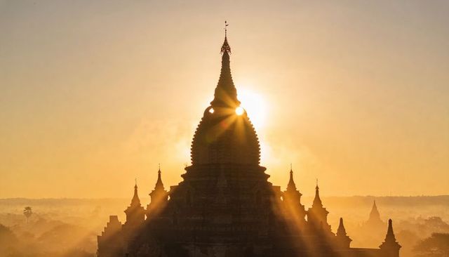 Sunburst piercing pagoda spire silhouette at golden dawn over misty bagan plain