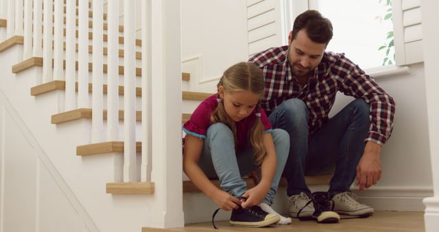 Happy caucasian father with daughter tying her shoes on stairs at home. Domestic life, family and lifestyle, unaltered.