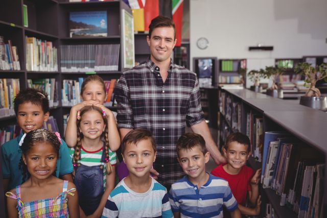 This image shows a happy teacher standing with a diverse group of schoolchildren in a library. They are all smiling and appear to be enjoying their time together. This image can be used for educational materials, school websites, promotional content for libraries, and articles about education and diversity.