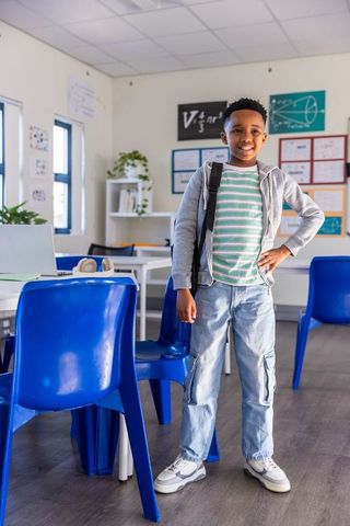 Confident african american student standing smiling with backpack in bright classroom