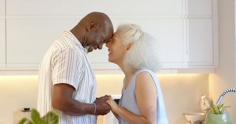 Senior couple holding hands in kitchen touching foreheads