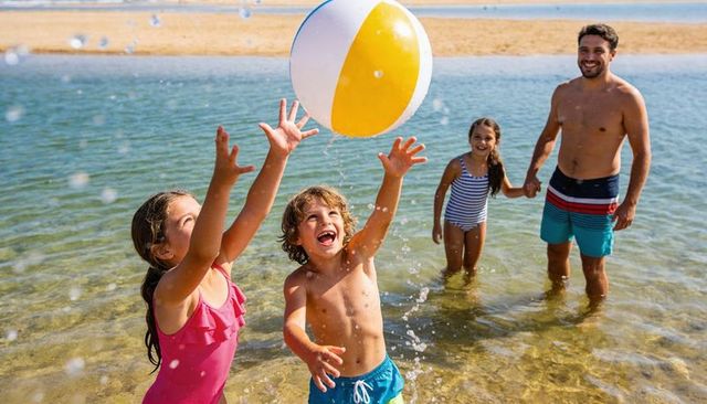 Family playing with giant beach ball in shallow coastal water on sunny summer day
