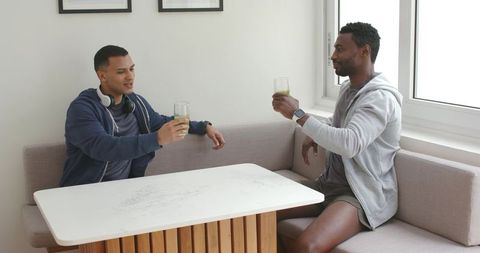 Friends clinking green drinks in bright minimalist dining nook by window, apartment toast