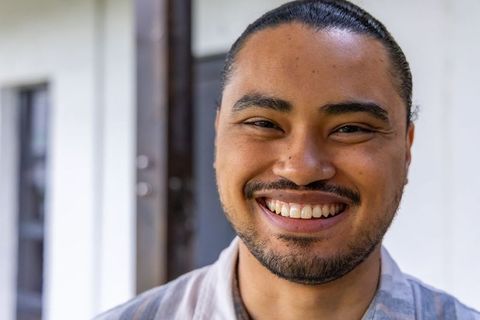 Asian man smiling on porch closeup, candid joyful portrait of young adult in striped shirt