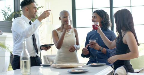 African american friends toasting with champagne and cocktails at modern kitchen counter