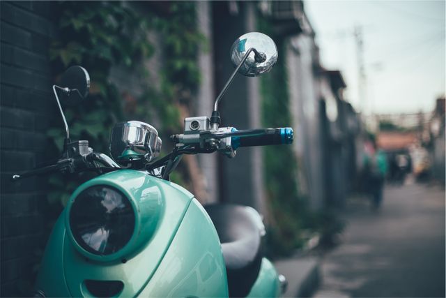 Vintage cyan scooter parked in a dimly lit narrow alleyway with blurred background. Suitable for urban exploration themes, travel promotions, transportation-related content, and retro lifestyle inspirations.