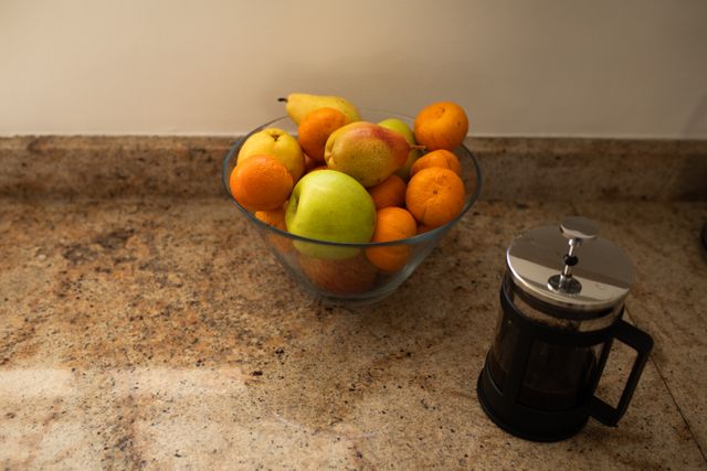 Close up of glass bowl filled with fruits apples, pears and mandarines and coffee maker on kitchen countertop.Domestic life interiors modern decor.