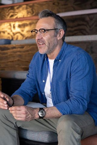 Middle-aged professional sitting in coworking lounge holding pen and wearing lanyard badge
