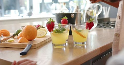 African american man preparing citrus drinks with strawberries and mint on wood counter