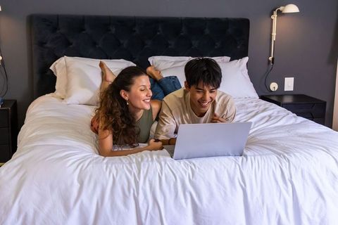 Young diverse couple relaxing on bed together using laptop for streaming and browsing