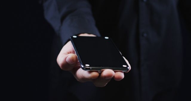 Hand of a caucasian man wearing a black shirt cradling a smartphone. mobile communication technology.