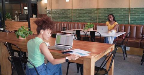 African american women working independently at communal wooden table in modern cafe coworking