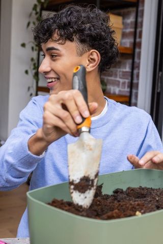 Smiling young asian gardener potting plants in homely garden