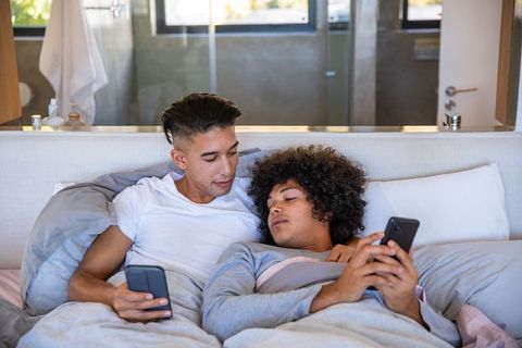 Intimate Male Couple Relaxing in Modern Bedroom with Smartphones