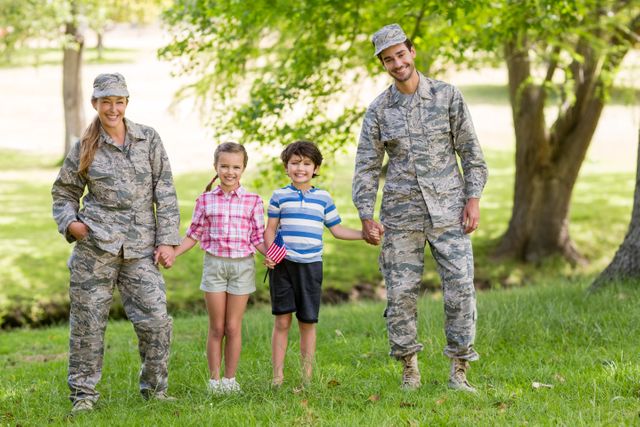 Military family spending quality time together in a park on a sunny day. Parents in uniform holding hands with their children, who are smiling and enjoying the outdoors. Ideal for use in articles about military families, patriotism, family bonding, and outdoor activities.