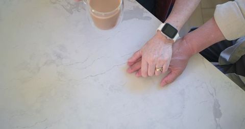 Diverse senior couple holding hands on marble kitchen counter with smartwatch and coffee
