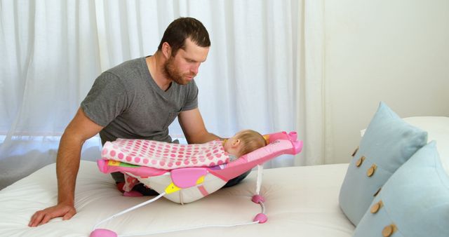 Caring Father Watching Over Resting Baby in Bouncer on Bed - Download Free Stock Images Pikwizard.com