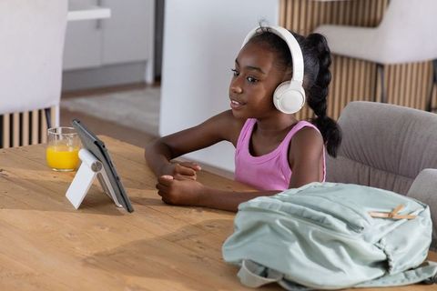 African american teen girl wearing headphones using tablet for remote learning at home