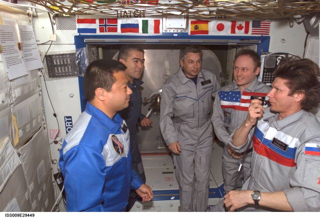 Astronauts and cosmonauts gather aboard the International Space Station's Destiny laboratory for a formal change-of-command ceremony, marking the transition from Expedition 9 to Expedition 10. The image captures the spirit of international cooperation and dedication of space agencies and their crew members. It can be used in educational material, publications focusing on space missions, teamwork, and international collaboration.