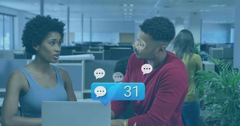 Colleagues collaborating at laptop in open-plan office showing message notification badge