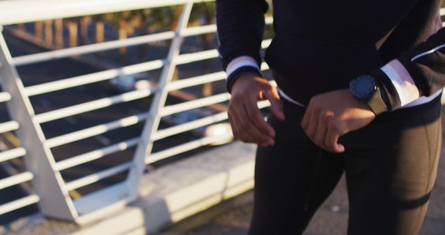 Midsection of african american man exercising on footbridge in city, checking smartwatch. fitness and active urban outdoor lifestyle.