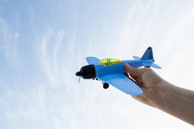 This image shows a hand holding a toy airplane against a clear blue sky, capturing the innocence and imaginative play of childhood. Ideal for use in advertisements for toys, children’s activities, and educational content about aviation. Can also be used in blogs and websites focused on parenting, childhood development, and outdoor play.