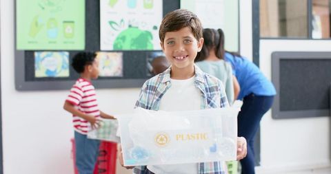 Smiling Boy Holding Plastic Recycling Bin in Classroom Promoting Sustainability