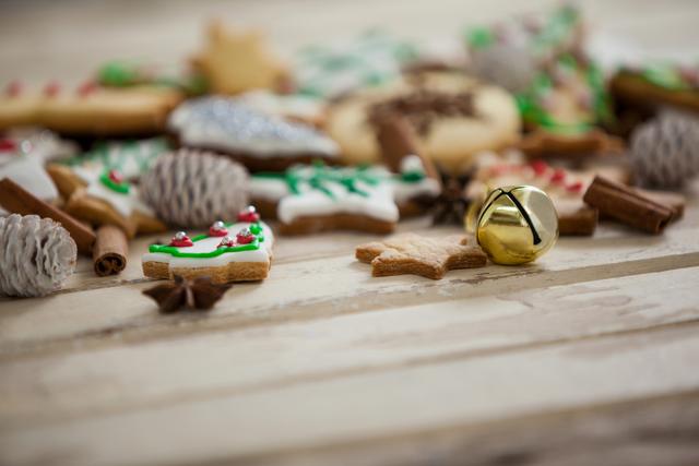 Christmas cookies with colorful icing and a golden jingle bell on a wooden plank. Cinnamon sticks, star anise, and pine cones add to the festive atmosphere. Ideal for holiday-themed promotions, Christmas cards, baking blogs, and festive event invitations.