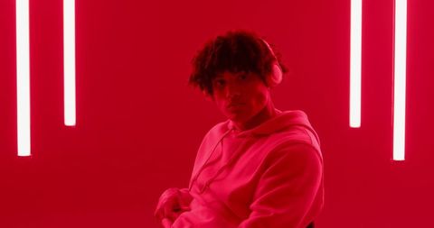 Asian Man in Red Lit Room with Neon Lights and Headphones