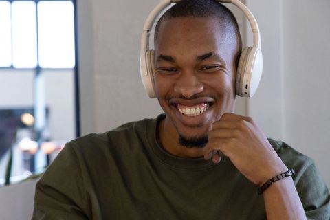 African american man smiling while wearing white wireless headphones at coworking desk