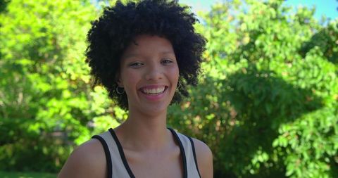 African american woman smiling in sunlit garden wearing tank and hoop earrings