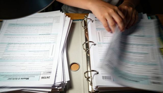 Hands Flipping Through Paperwork in Three-Ring Binder with Stacked Forms and Barcode